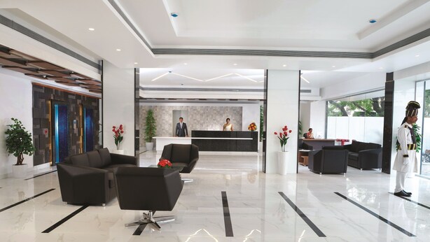 Un moderno vestíbulo de hotel con una recepción, zona de estar y un amplio ventanal que proporciona luz natural.