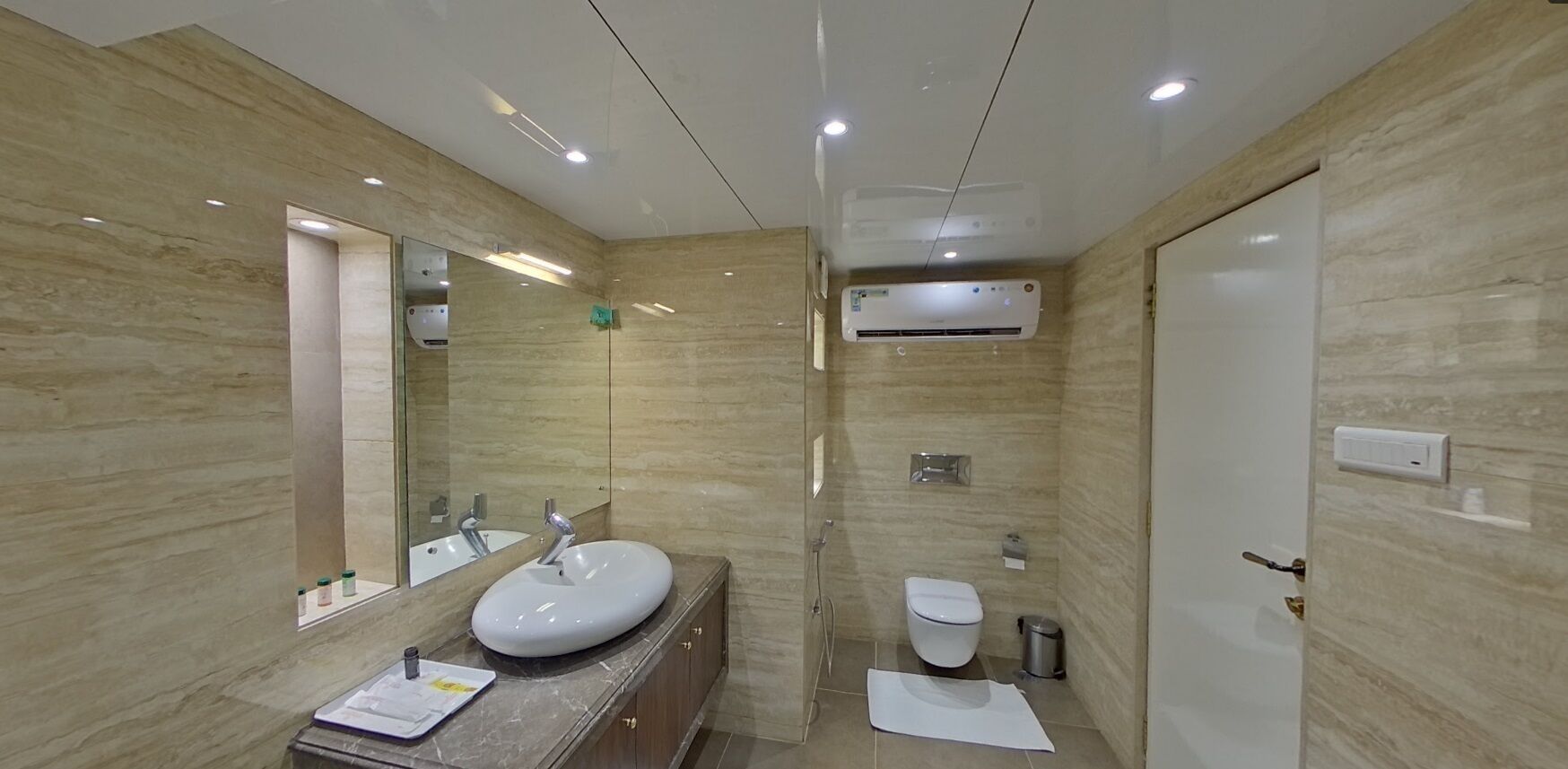 A modern bathroom with a marble vanity, a large mirror, a toilet, and an air conditioning unit.