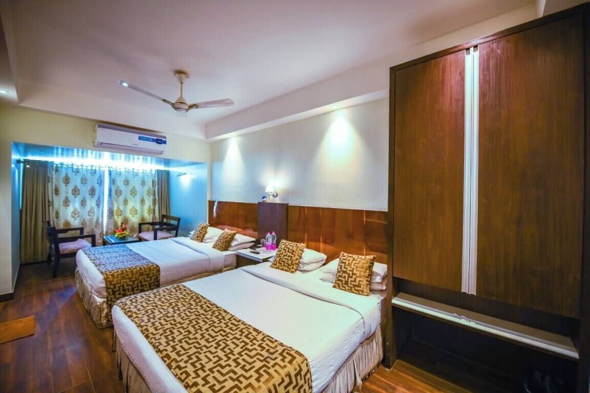 Une chambre d’hôtel avec deux lits, un ventilateur de plafond, un appareil de climatisation, un bureau avec une chaise et une grande armoire.