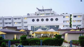 A modern hotel with a central courtyard, outdoor seating, and a sign indicating it is a holiday resort.