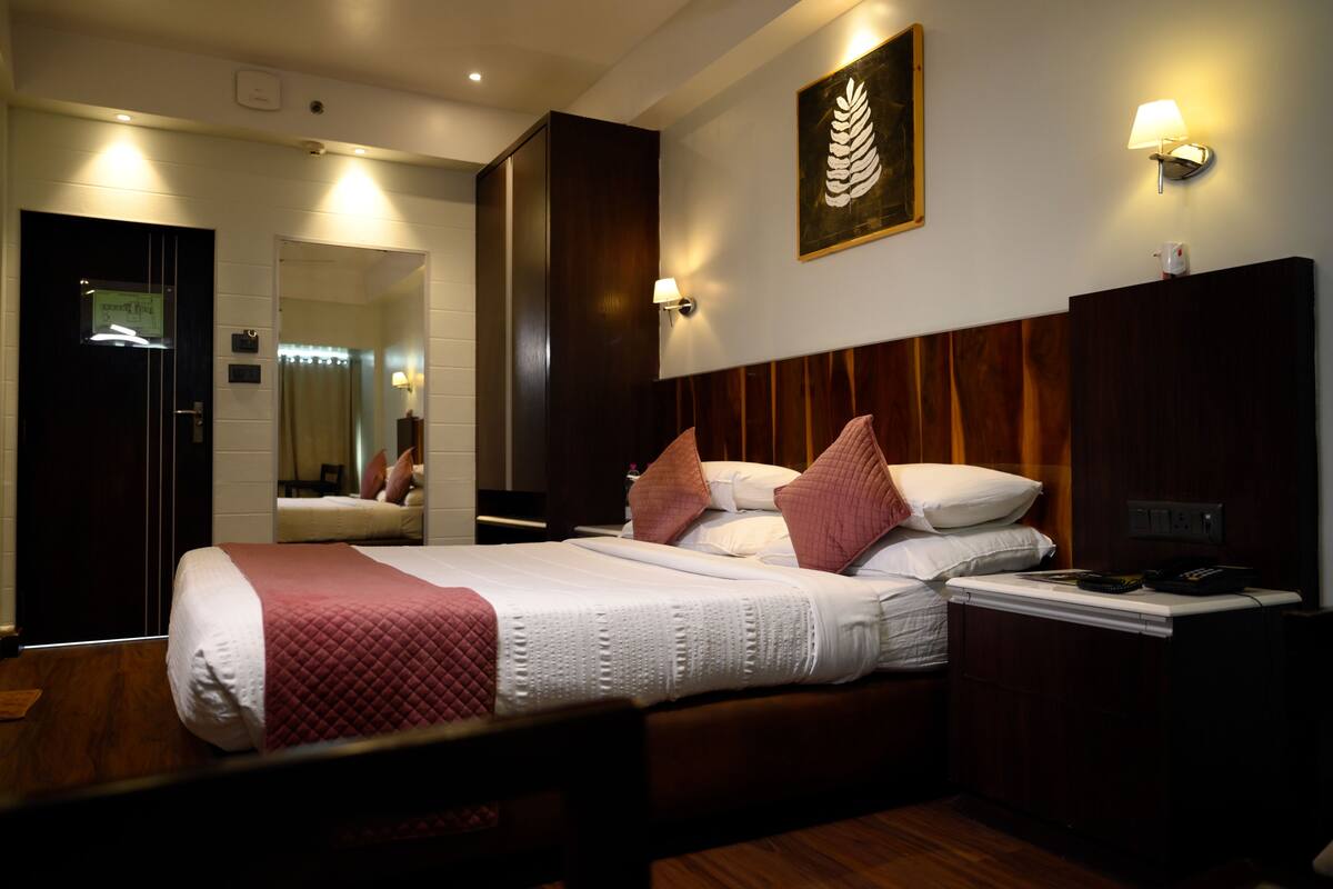 Une chambre d’hôtel avec un grand lit, une tête de lit en bois, une table de chevet, un miroir et une lampe fixée au mur.