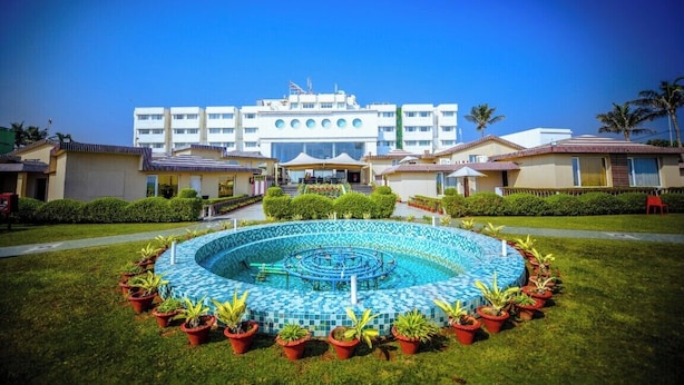 Un hôtel doté d’une piscine centrale, entourée de plantes en pot, d’une pelouse bien entretenue et surplombant un ciel bleu azur.