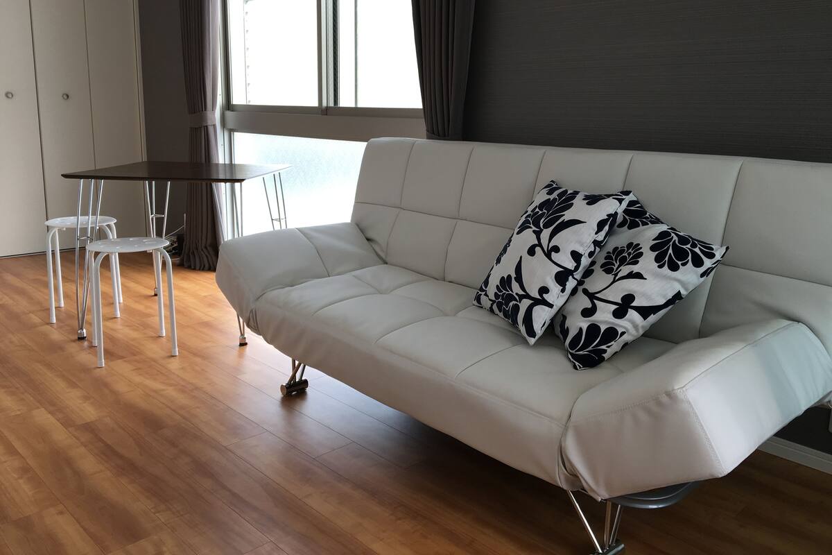 A modern living room with a white sofa, two white chairs, a small table, and a large window with curtains.