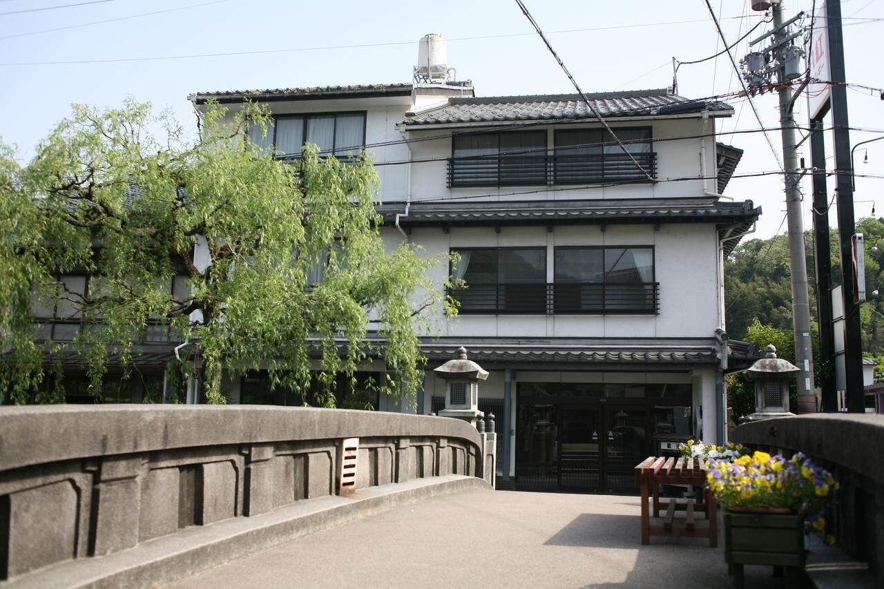 A traditional Japanese building with a two-story structure, a tiled roof, and a small garden area with a wooden bench and potted plants.