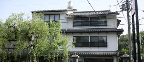 A traditional Japanese building with a two-story structure, a tiled roof, and a small garden area with a wooden bench and potted plants.