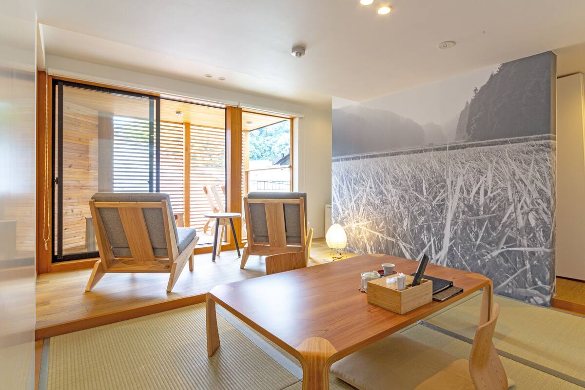 A modern room with a wooden table, chairs, a laptop, and a wall with a nature mural.