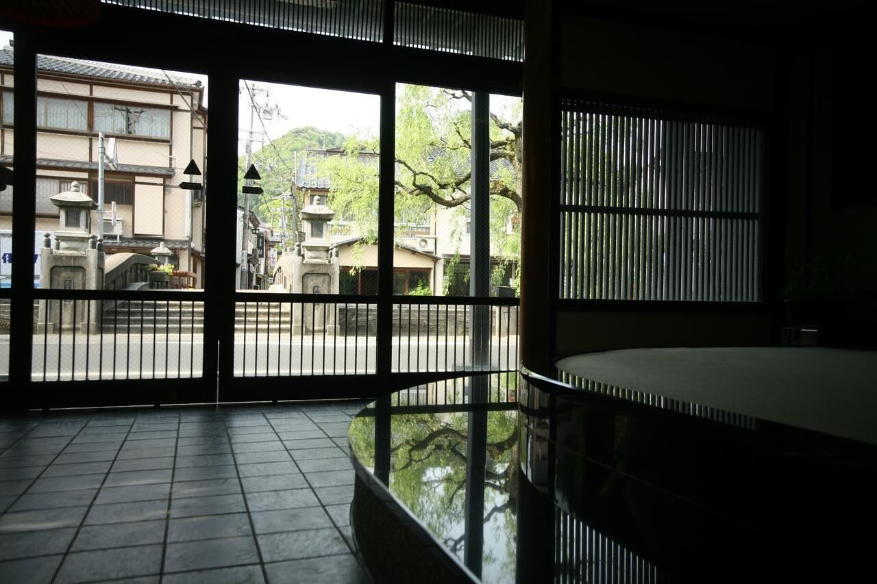 Una habitación japonesa tradicional con suelo de tatami, una mesa baja y una puerta corrediza que da a un patio con edificios tradicionales y un farol de piedra.