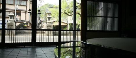 Una habitación japonesa tradicional con suelo de tatami, una mesa baja y una puerta corrediza que da a un patio con edificios tradicionales y un farol de piedra.