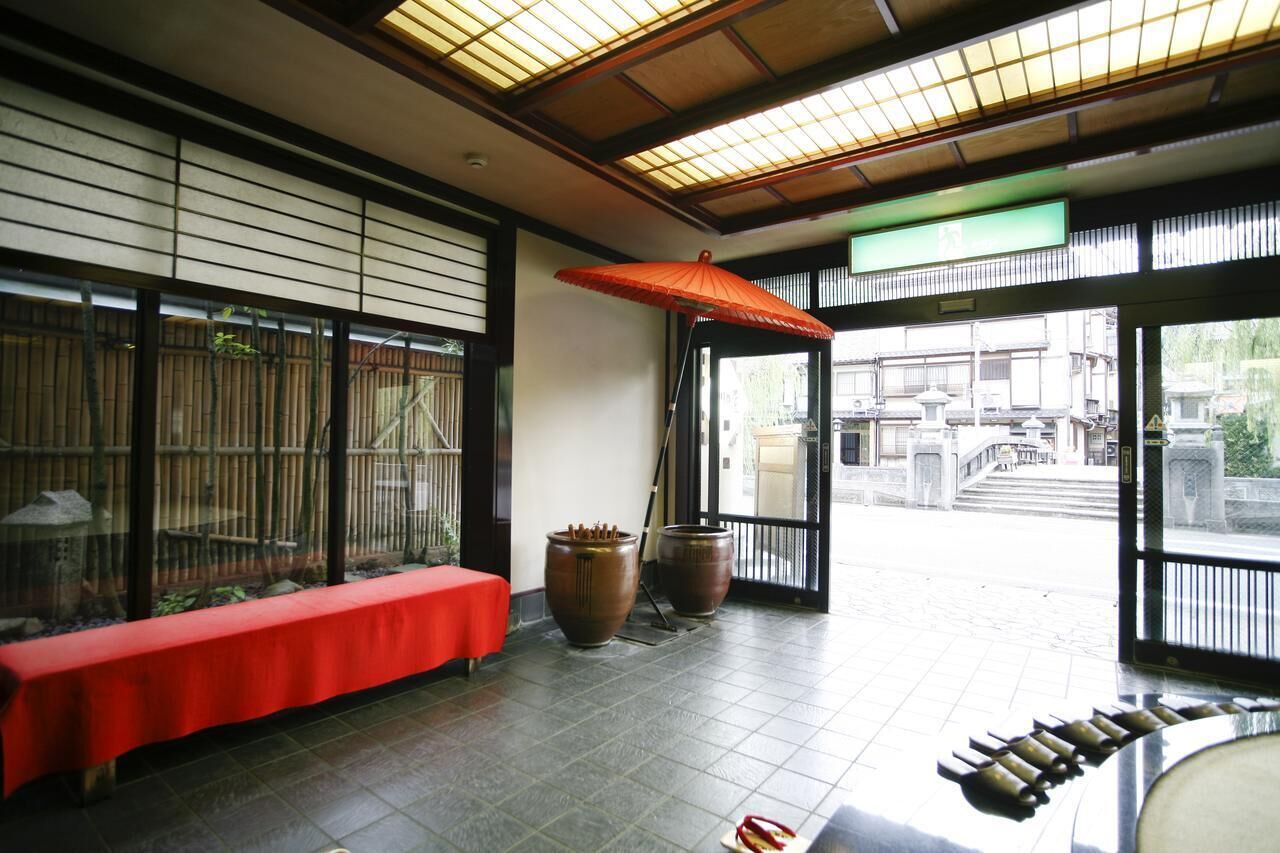 Et traditionelt japansk rum med tatamimåtter, en rød bænk, store keramikvaser og en skydedør, der fører til et udendørs område.