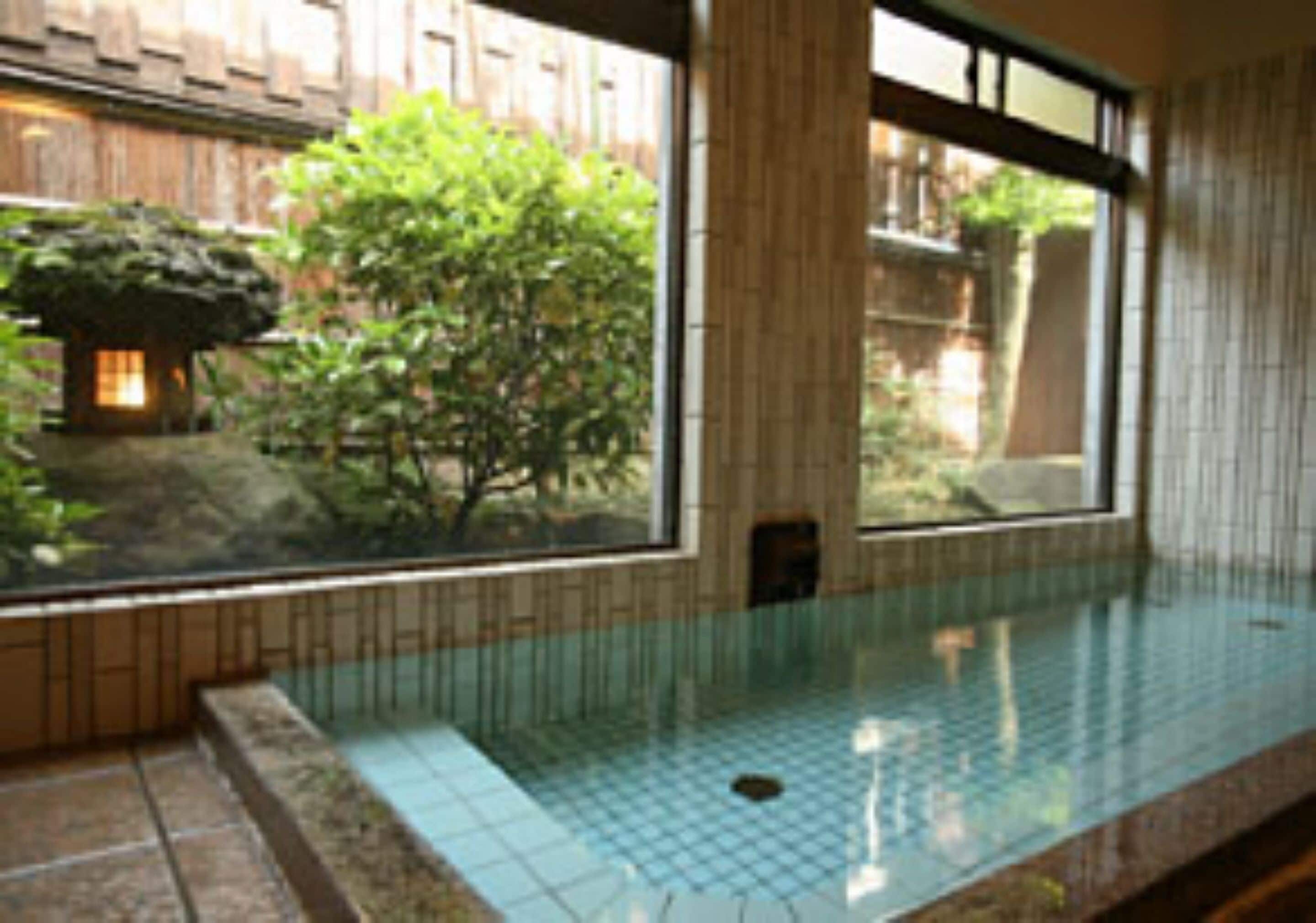 Una habitación con un gran ventanal, suelo de baldosas y un pequeño jardín interior a la vista a través de la ventana.