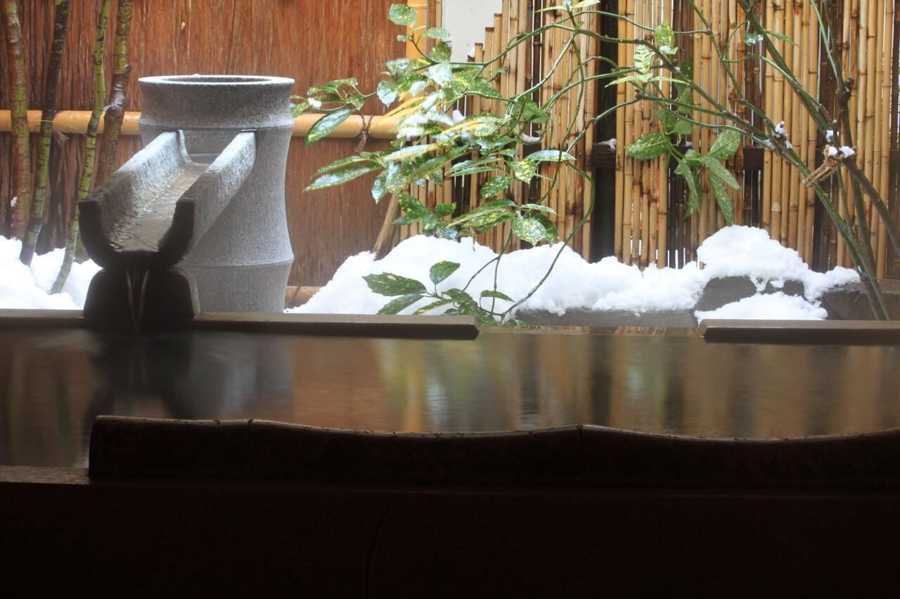 A traditional Japanese garden with a stone water feature, bamboo fence, and a snow-covered ground.