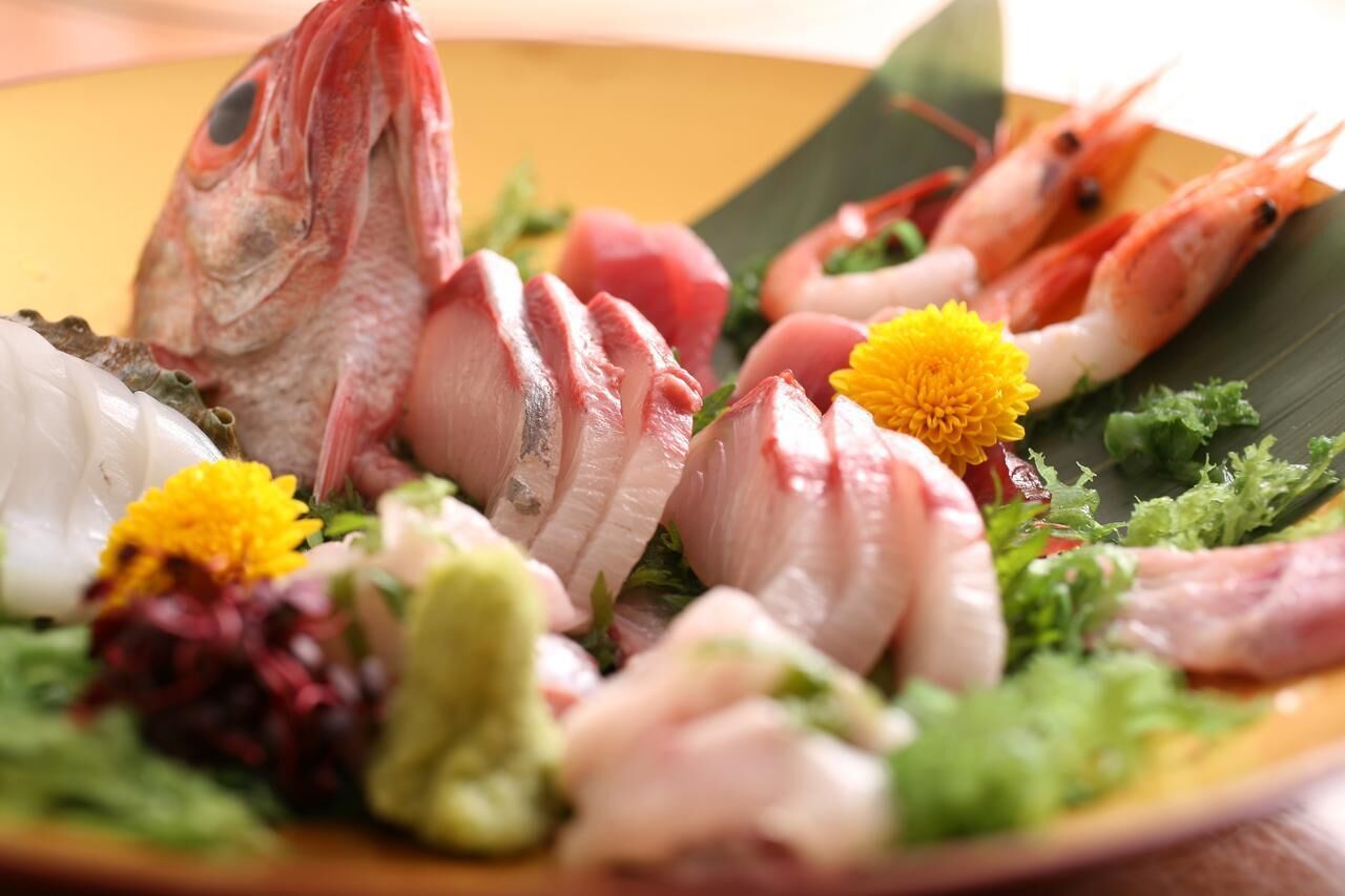 A plate of seafood including fish, shrimp, and squid, garnished with flowers and greens.