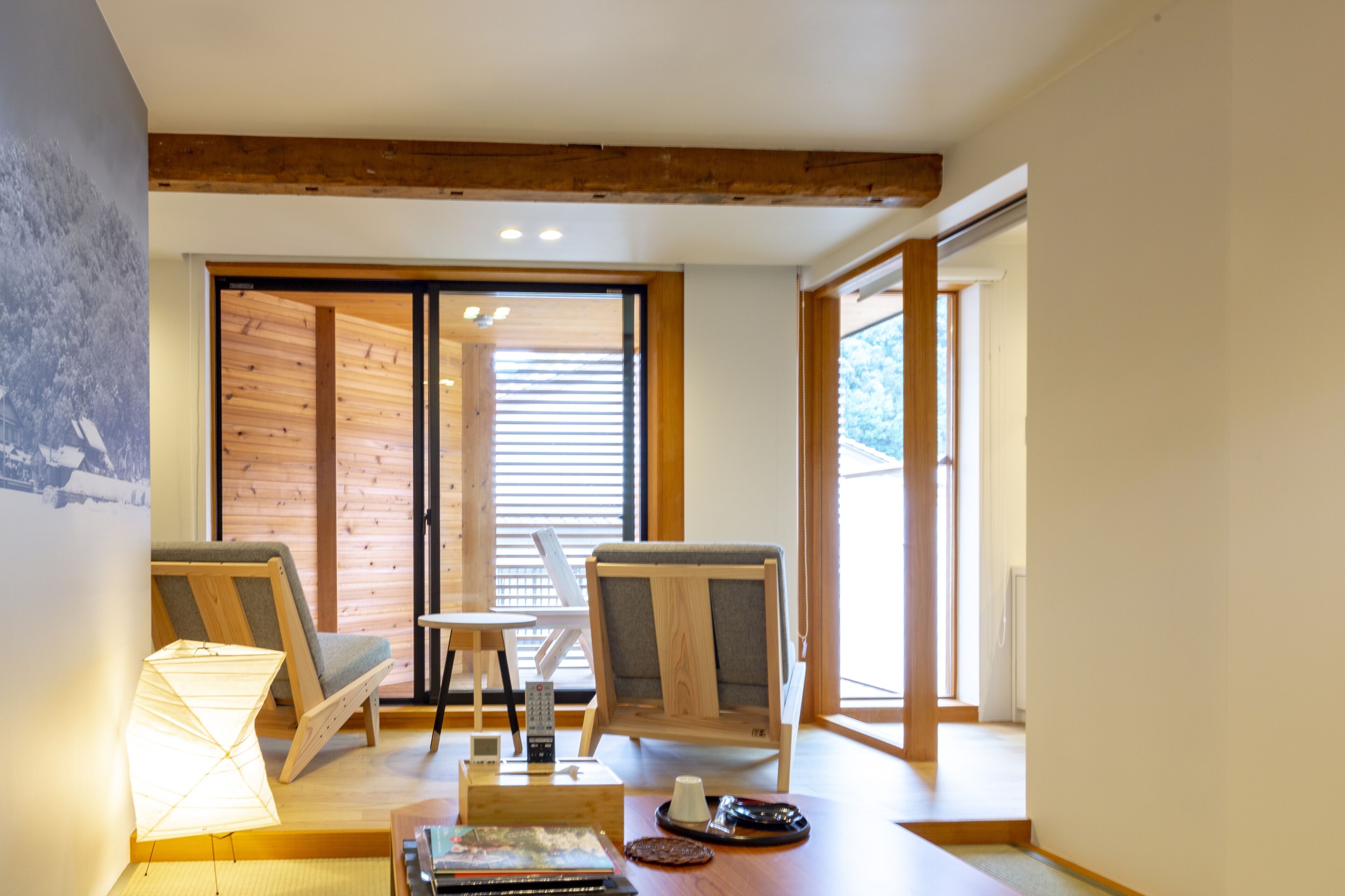 Una habitación con techo de madera, puerta corredera y vistas al exterior. Hay dos sillas, una mesa y una lámpara.