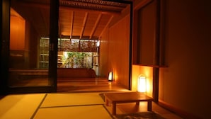 Una habitación japonesa tradicional con suelo de tatami, una mesa de madera baja y una puerta corredera que da a un jardín.