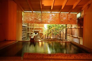 Un onsen japonés tradicional con interior de madera, una fuente termal de piedra y plantas de bambú.