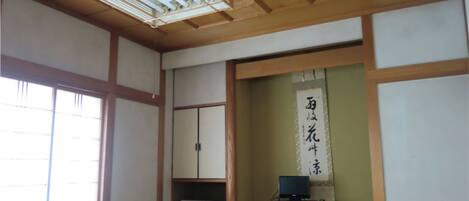 Una habitación japonesa tradicional con suelo de tatami, una puerta corredera, un televisor sobre un pequeño soporte y un ventilador de techo.