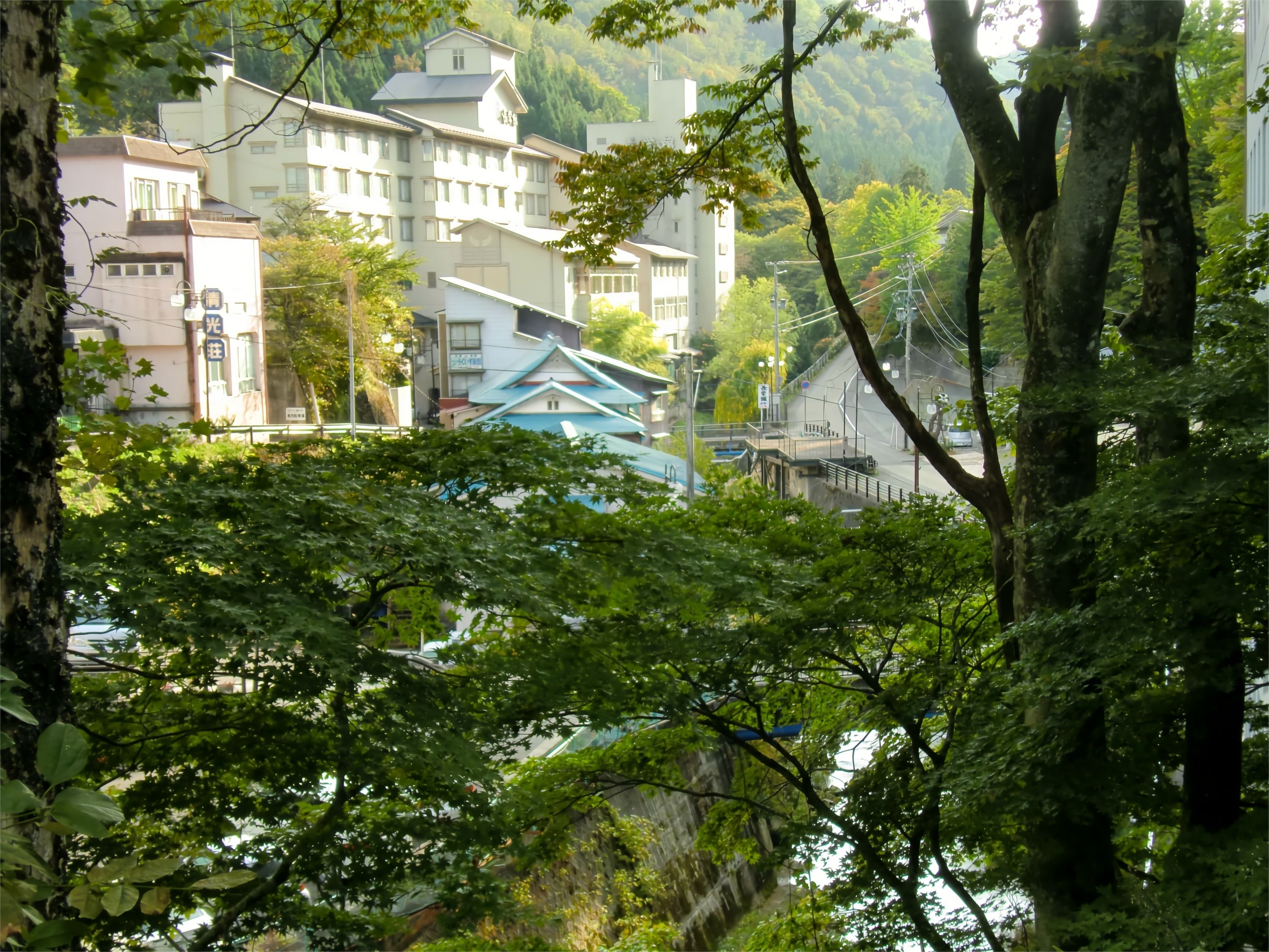 A traditional Japanese building with multiple stories, surrounded by lush greenery and a river.
