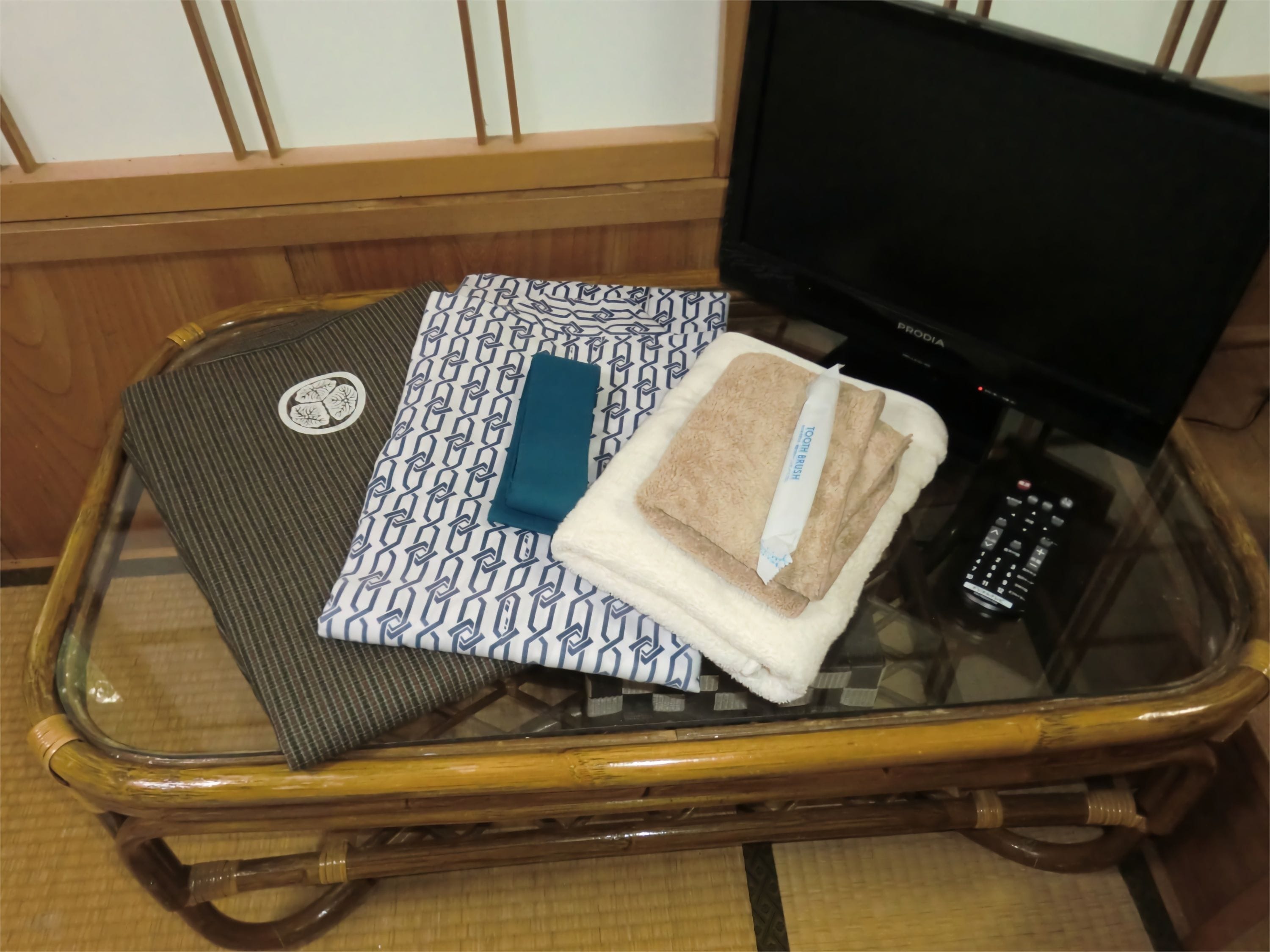 A glass-top table with a woven mat, a patterned pillow, a folded towel, and a remote control.