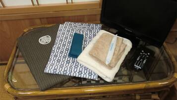 A glass-top table with a woven mat, a patterned pillow, a folded towel, and a remote control.