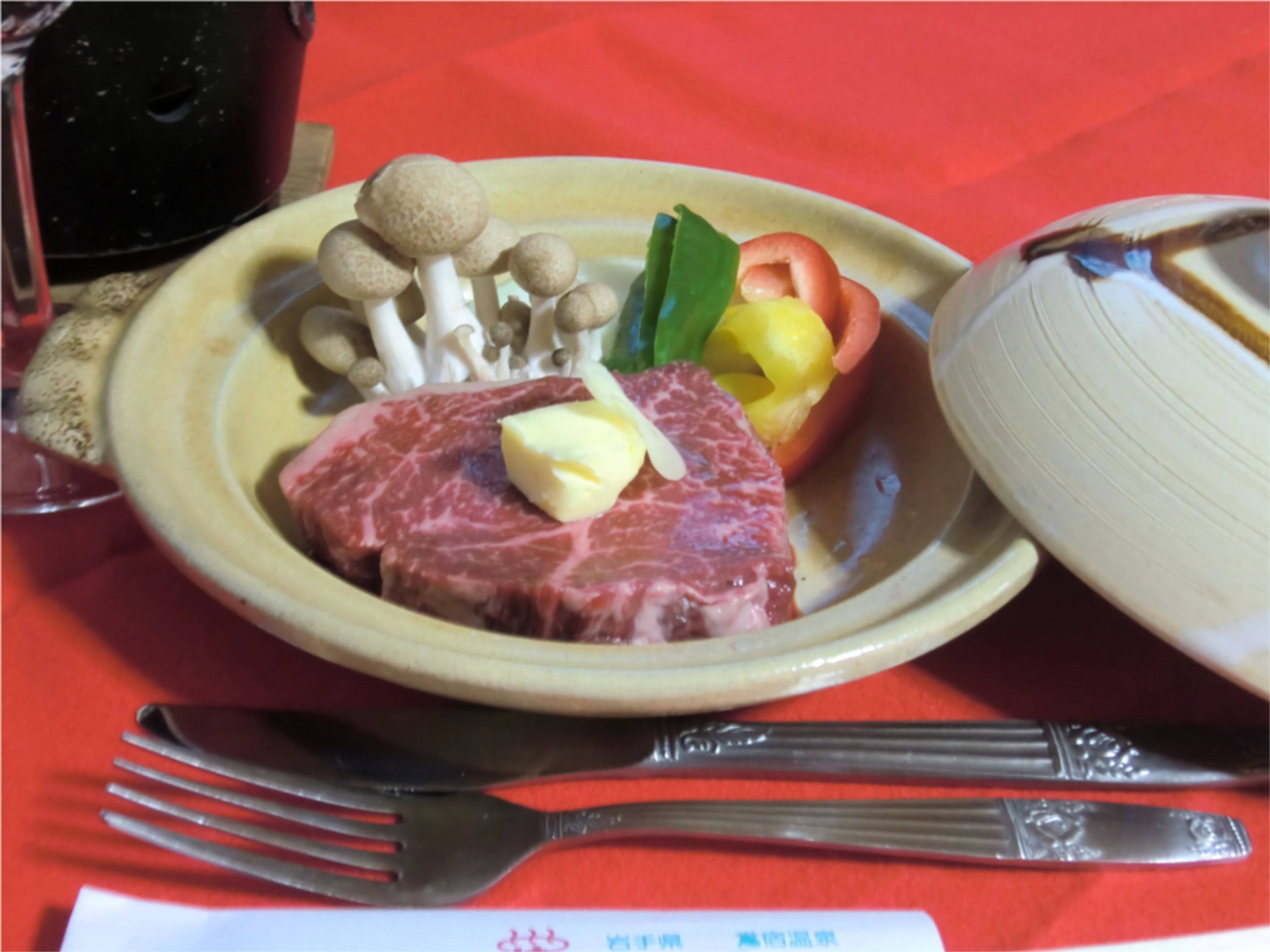 A plate with steak, mushrooms, bell peppers, and a tomato on a red tablecloth.