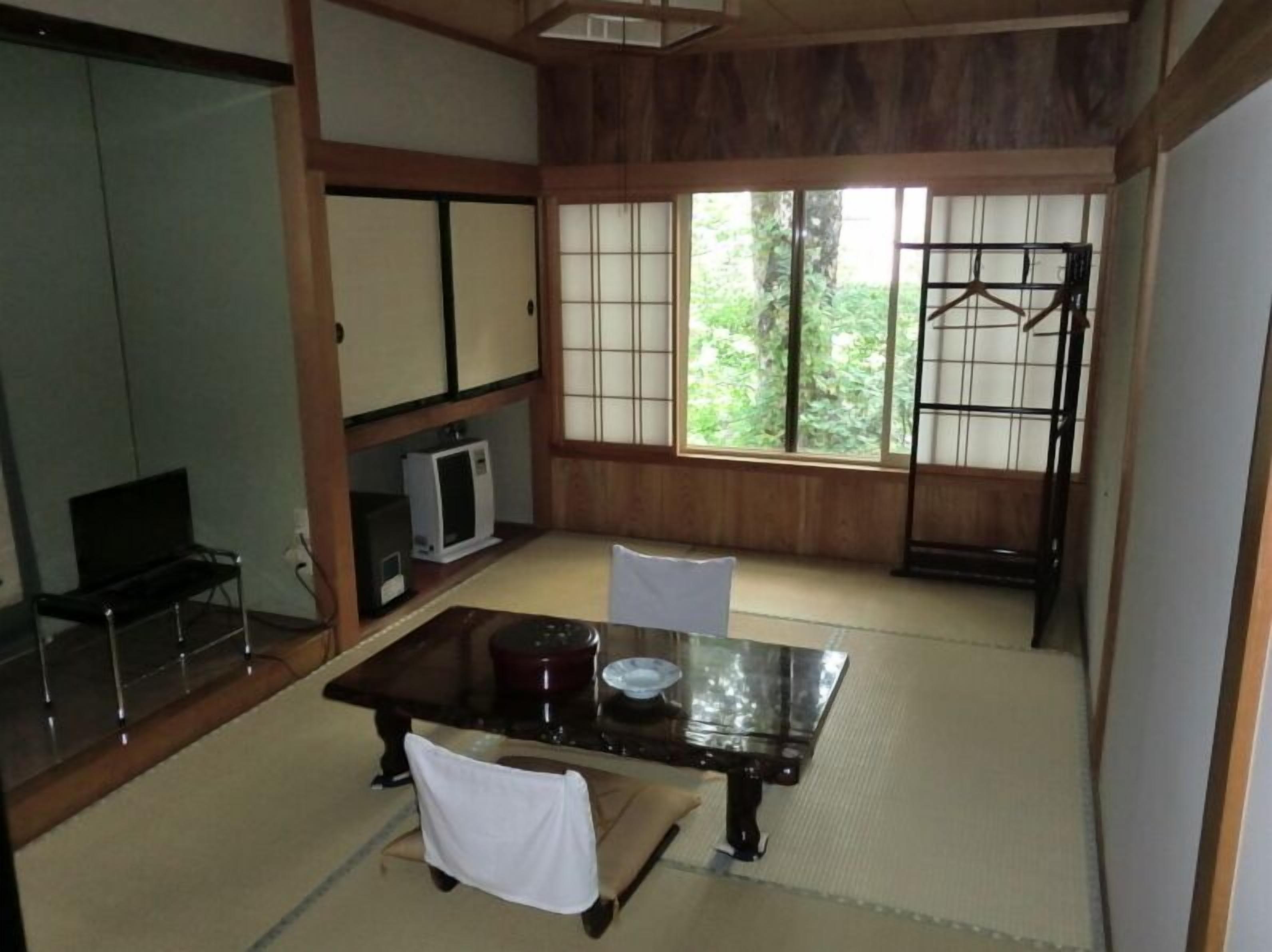 Una habitación japonesa tradicional con suelo de tatami, una mesa baja, un televisor y puertas correderas.