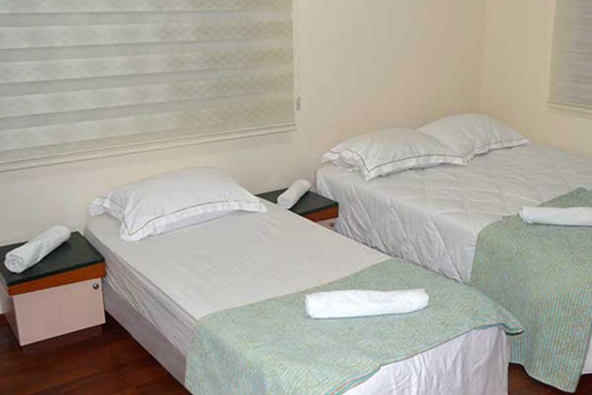 Une chambre avec deux lits simples, chacun équipé d’un oreiller et d’une serviette enroulée. Une petite table avec un téléphone et un livre se trouve à côté de l’un des lits.