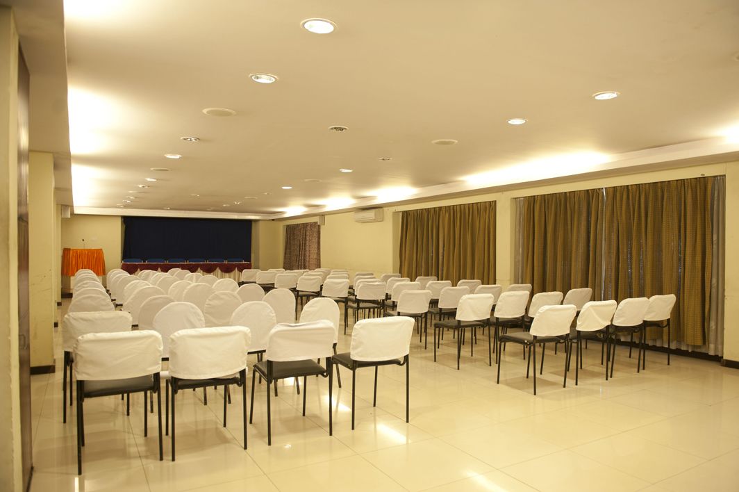 A conference room with rows of chairs, a projector screen, and curtains.