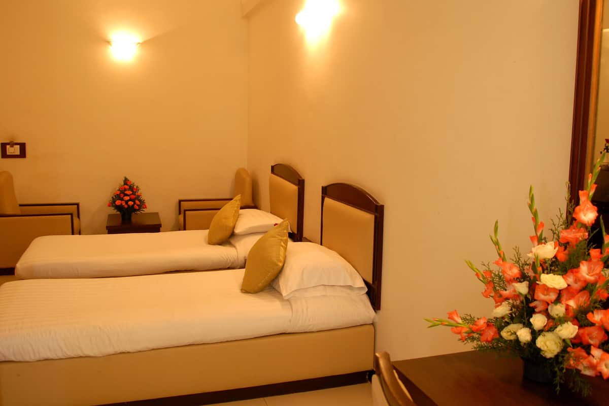 Habitación de hotel con dos camas individuales, una mesita de noche con un florero y una mesa de madera.