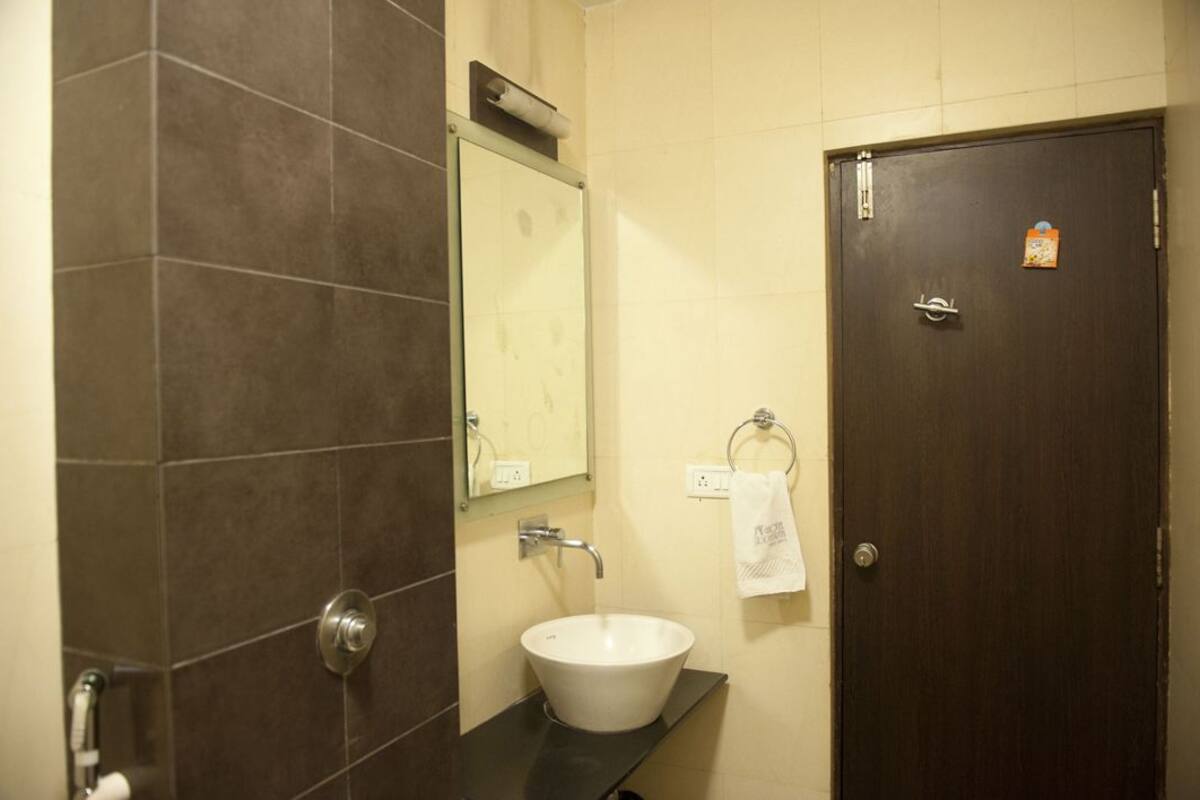 Un baño con un lavabo blanco, azulejos marrón oscuro, un espejo y una puerta con cerradura.