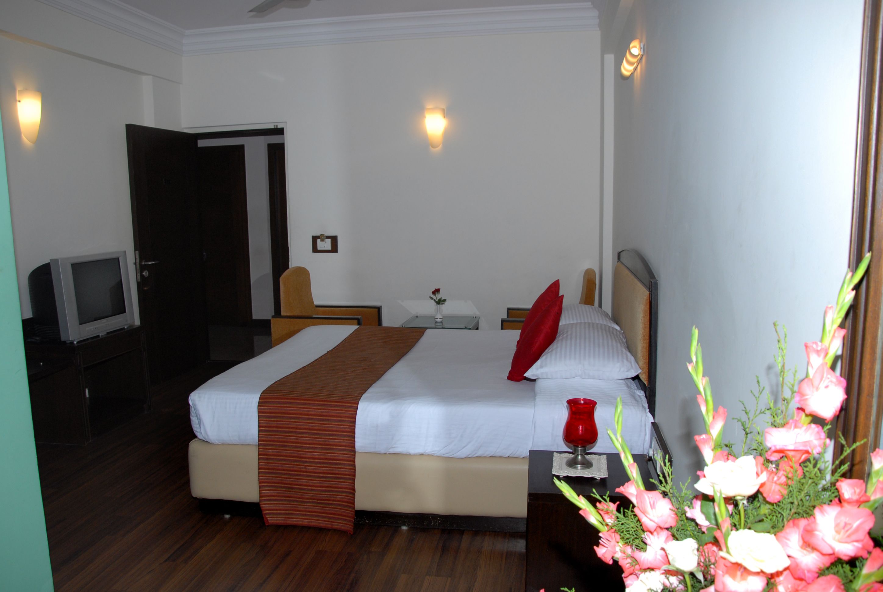 A hotel room with a bed, bedside table, lamp, and a television.