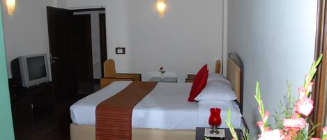 A hotel room with a bed, bedside table, lamp, and a television.