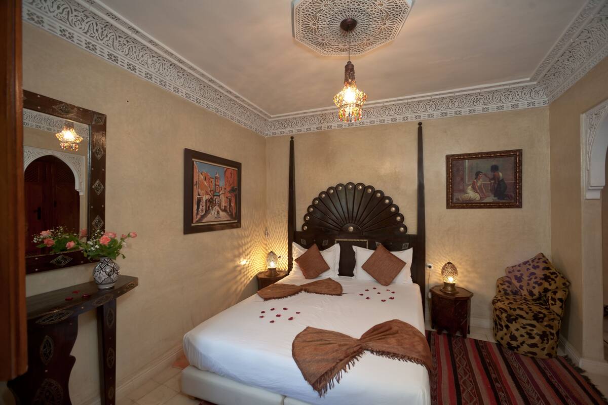 Una habitación de hotel bien decorada con una cama grande, un techo ornamentado y arte tradicional.