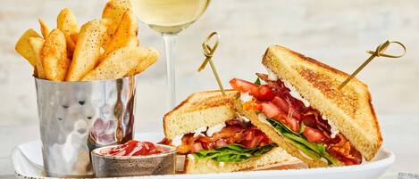 A plate with a grilled sandwich, a glass of white wine, and a container of fries.