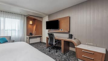 A hotel room with a bed, a desk with a chair, a television, and a small kitchenette area.