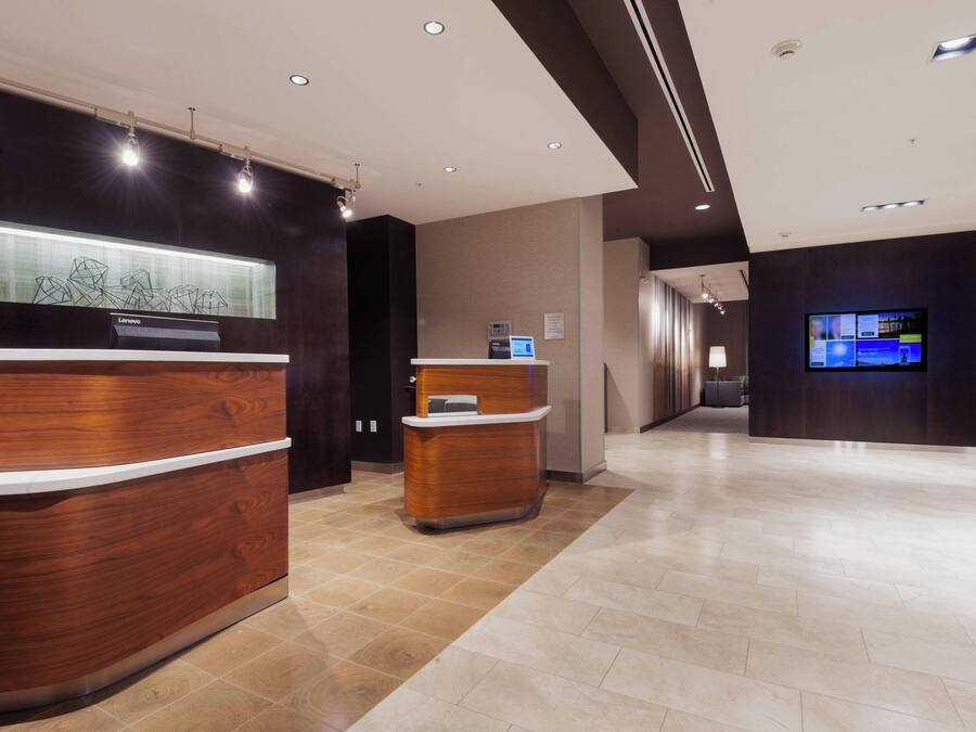 A modern hotel reception area with a wooden reception desk, a digital display, and a television screen.