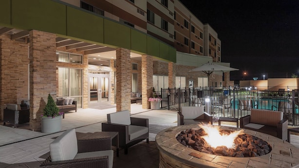 An outdoor patio area with stone pillars, wicker furniture, a fire pit, and a pool in the background.