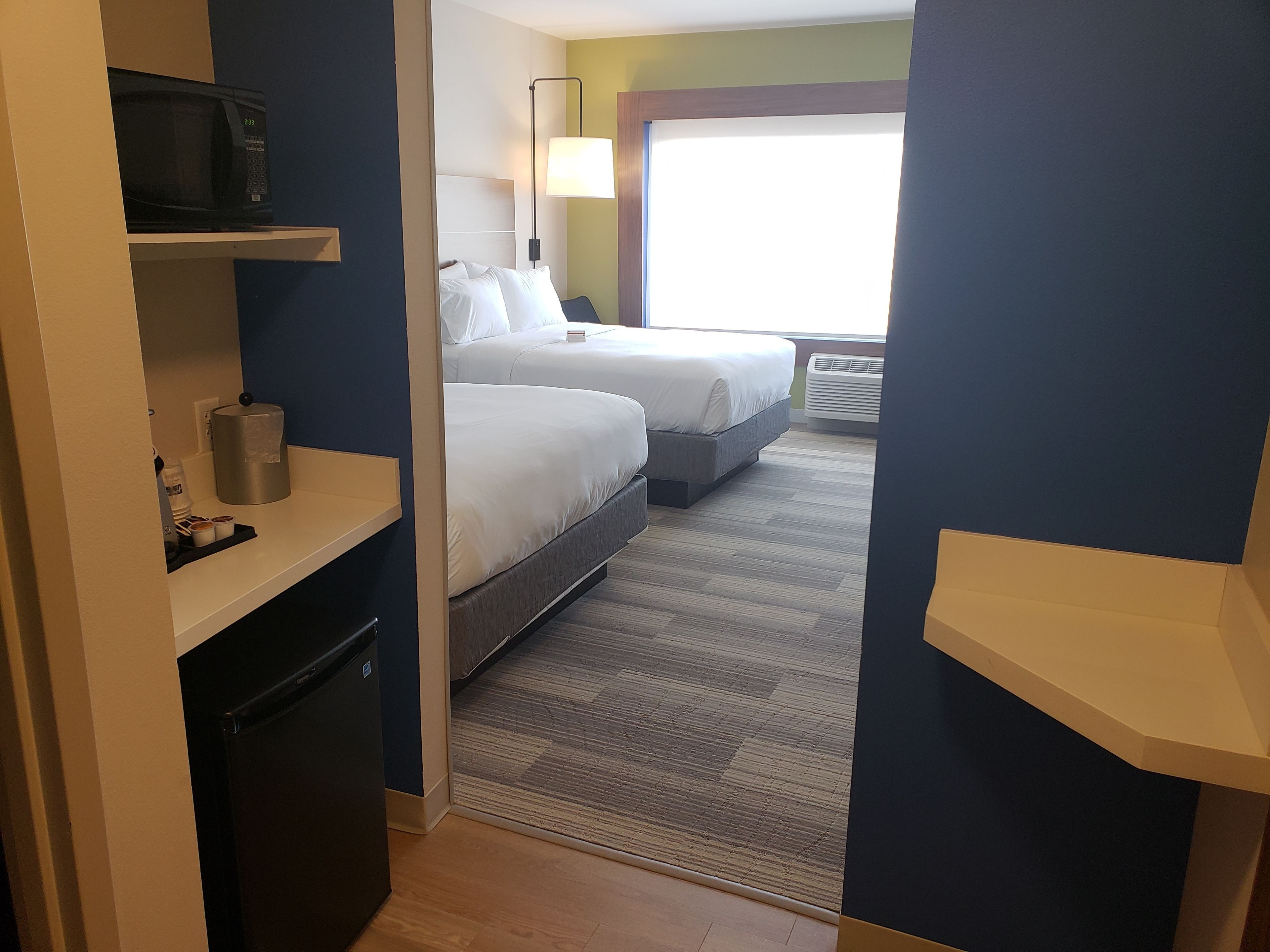 A hotel room with two beds, a microwave, a coffee machine, and a small refrigerator.