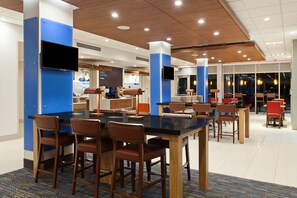 A modern dining area with a long table, multiple chairs, and a television mounted on a blue pillar. - Holiday Inn Express & Suites Brigham City - North Utah by IHG (Brigham City)
