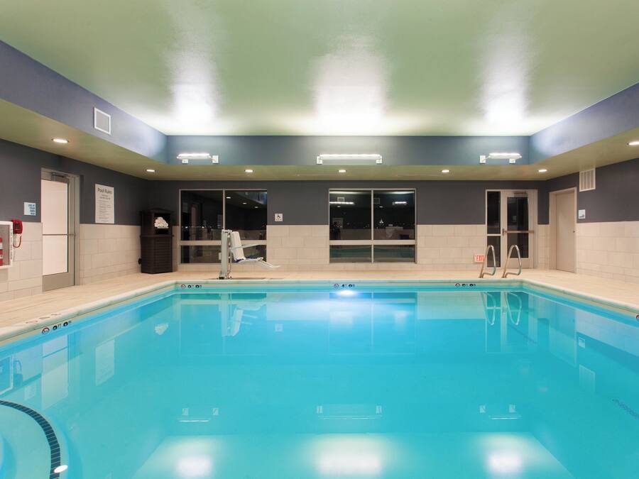 Una piscina con agua cristalina, rodeada de muros con una combinación de colores oscuros y claros, y equipada con señales de seguridad y salidas.