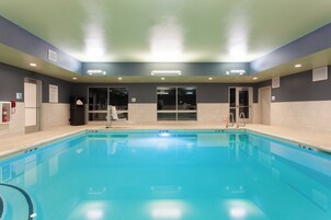 Una piscina con agua cristalina, rodeada de muros con una combinación de colores oscuros y claros, y equipada con señales de seguridad y salidas.