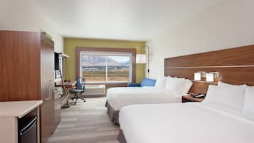 A hotel room with two beds, a desk, a chair, and a view of mountains.