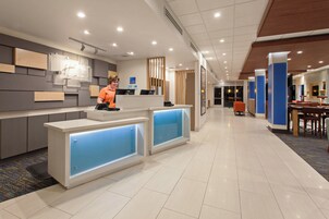 Zona de recepción moderna de un hotel, con una recepcionista, mostrador de recepción y área de espera con asientos.