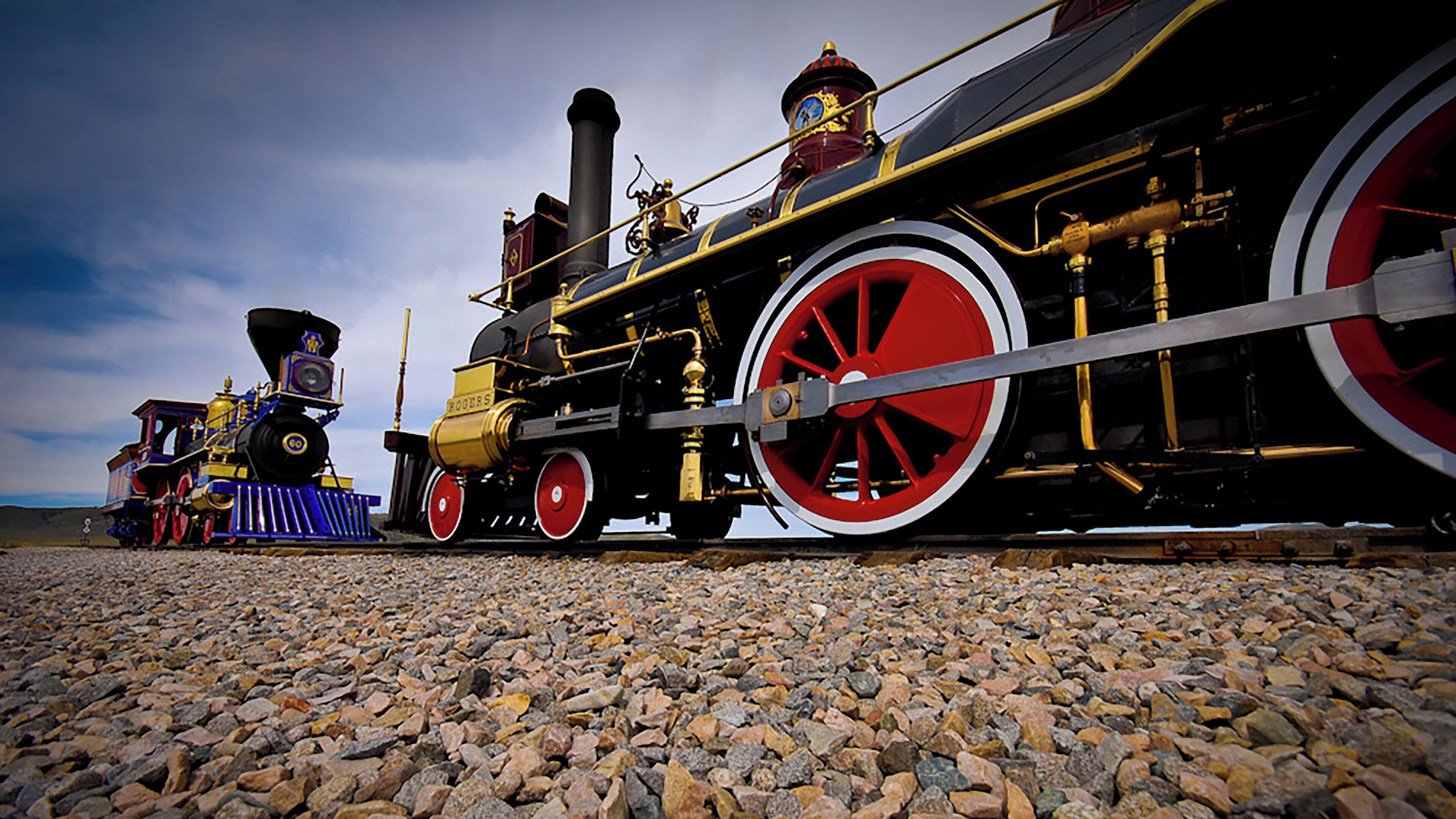 A steam locomotive with red wheels and a black body, positioned on a gravel track.