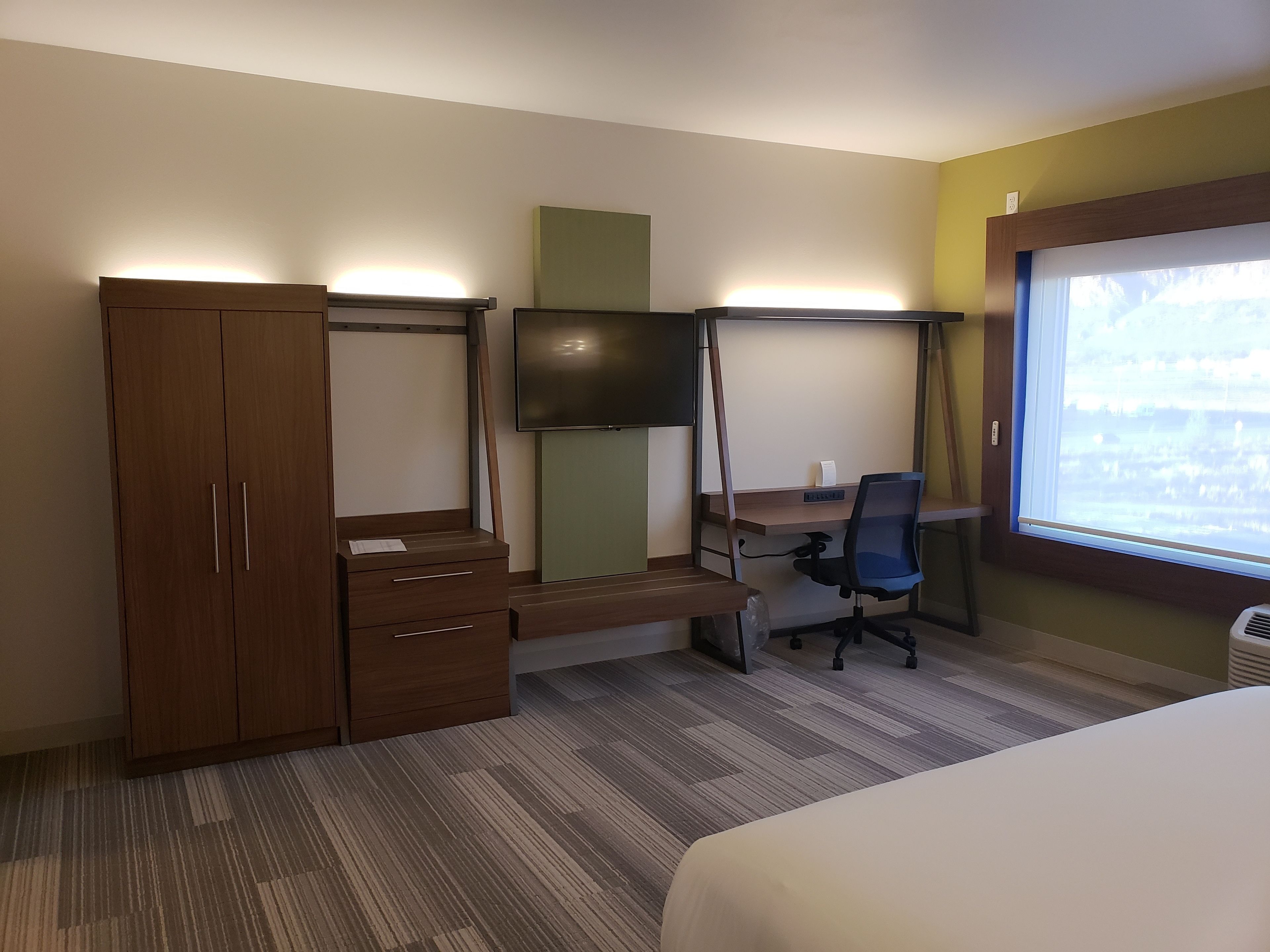 Habitación de hotel con cama, escritorio con silla, televisor, armario y ventana con vistas.