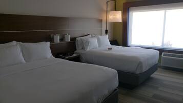 Ein Hotelzimmer mit zwei Betten, einem Nachttisch, einer Lampe und einem Fenster mit Blick.