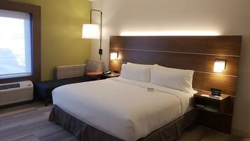Een hotelkamer met een groot bed, nachtkastjes, een lamp en een raam met jaloezieën.