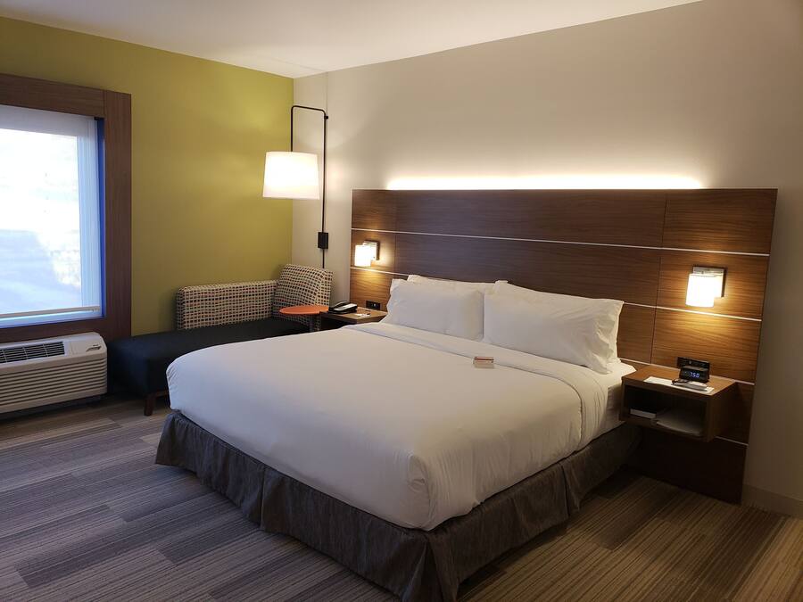 Een hotelkamer met een groot bed, nachtkastjes, een lamp en een raam met jaloezieën.