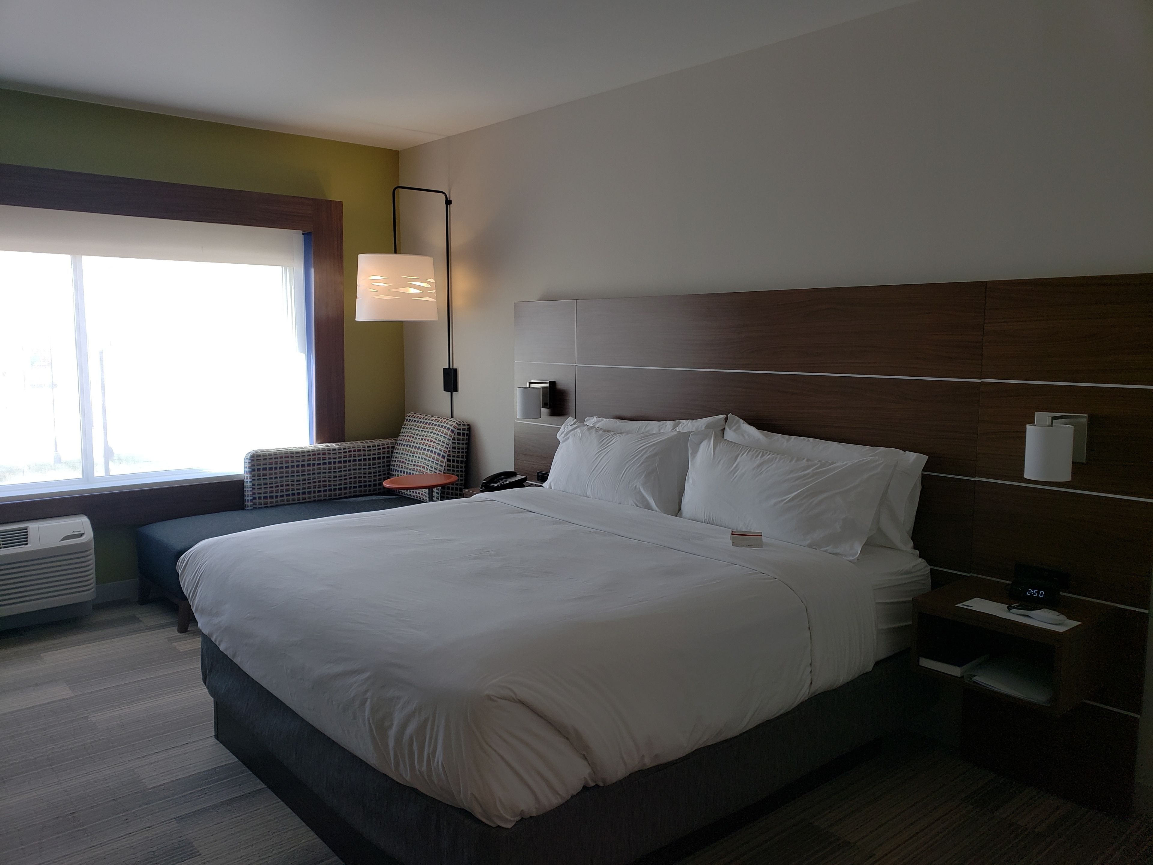 Hotellihuone, jossa on suuri sänky, yöpöydät, yövalaisin, lamppu, tuoli ja ikkuna.