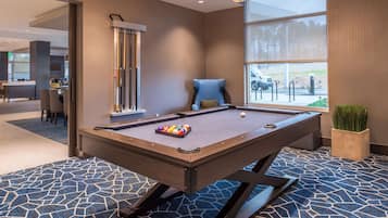 A pool table with balls, a blue armchair, and a large window with a view of the outside.
