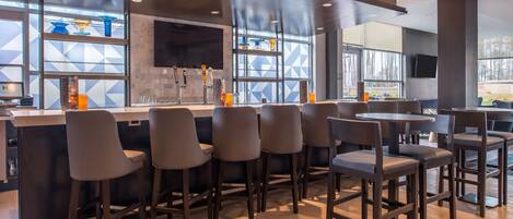 A modern bar area with high stools, a counter, and a large window with geometric patterns.